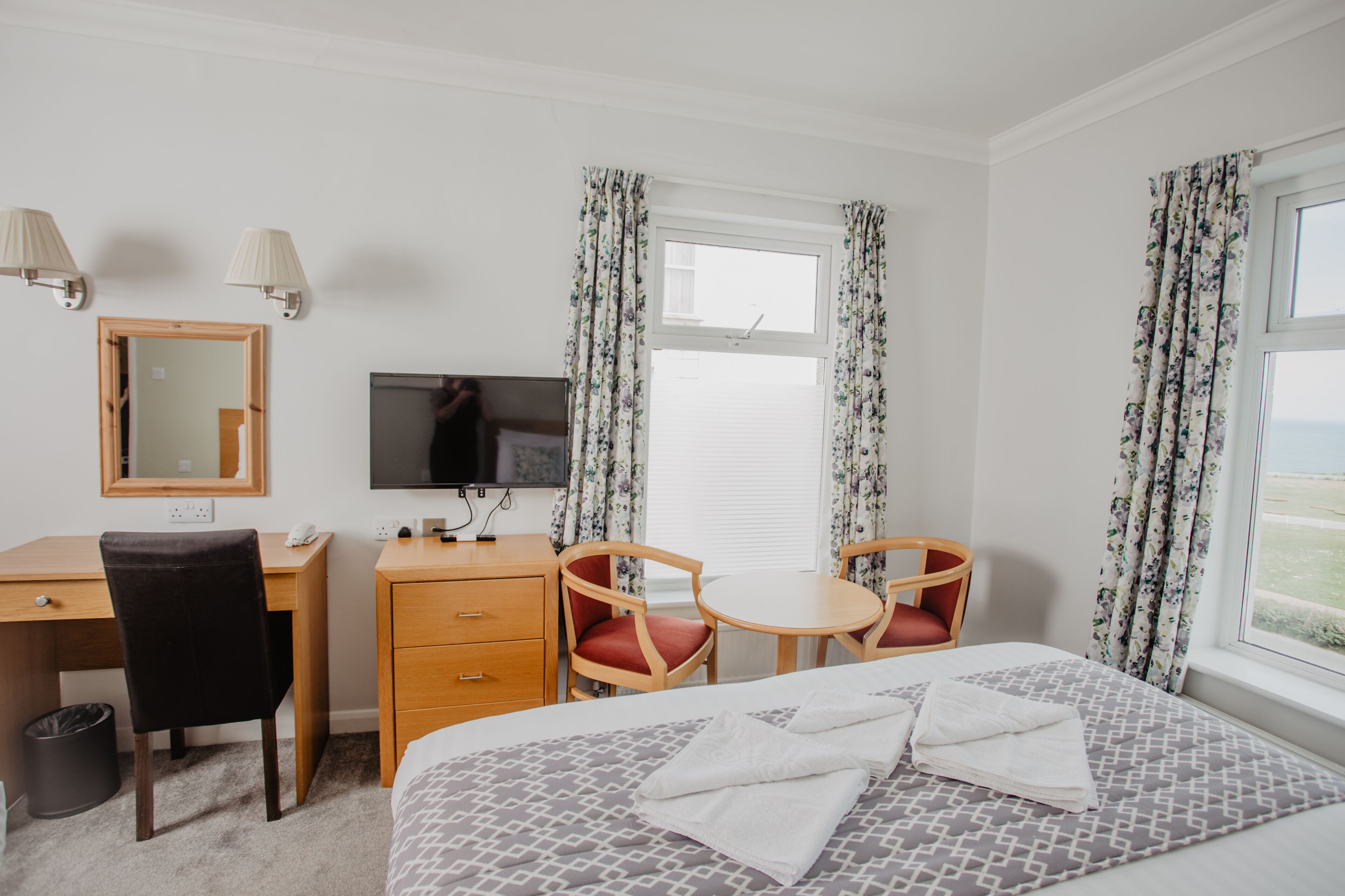 Habitación de hotel con cama, escritorio, sillas, televisor y ventana con cortinas.