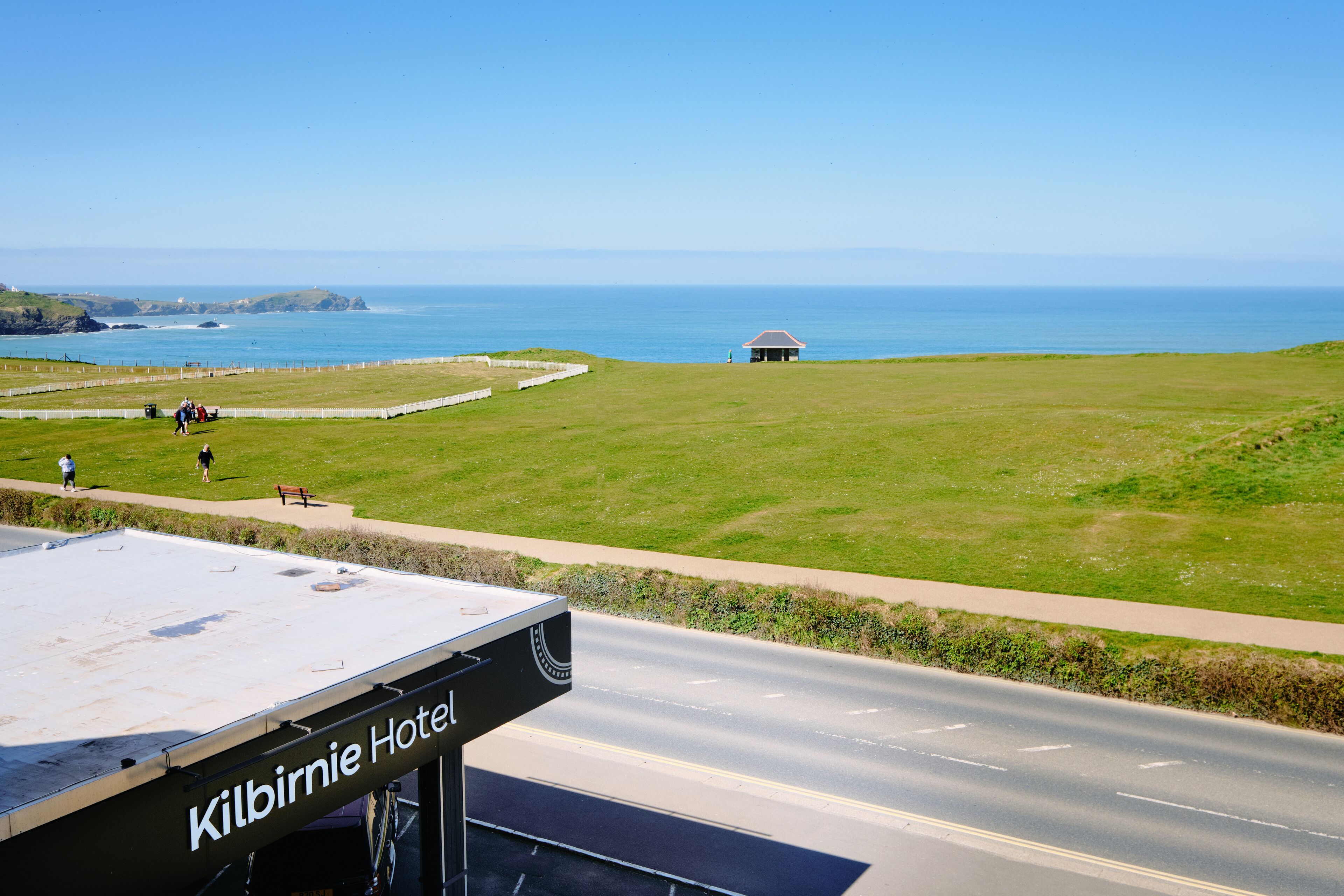 Blick auf das Kilbirnie Hotel, im Vordergrund eine Straße, eine Grünfläche und im Hintergrund das Meer.