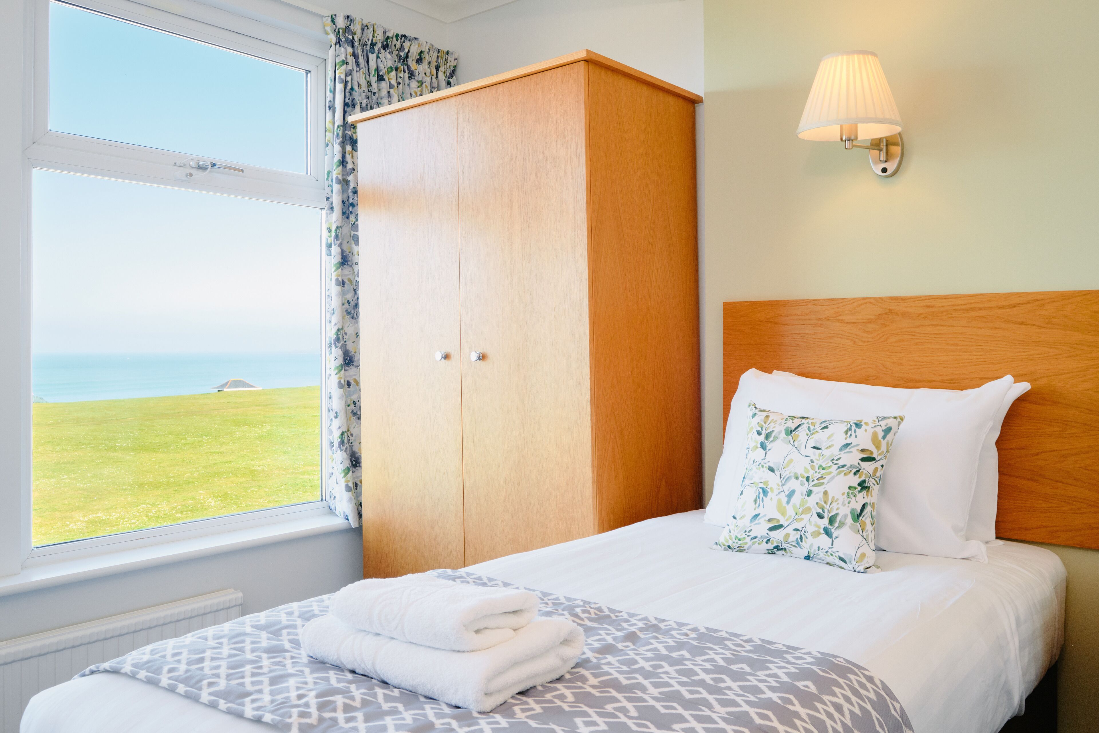 Ein Schlafzimmer mit Bett, Kleiderschrank, Fenster mit Meerblick und einer Wandlampe.
