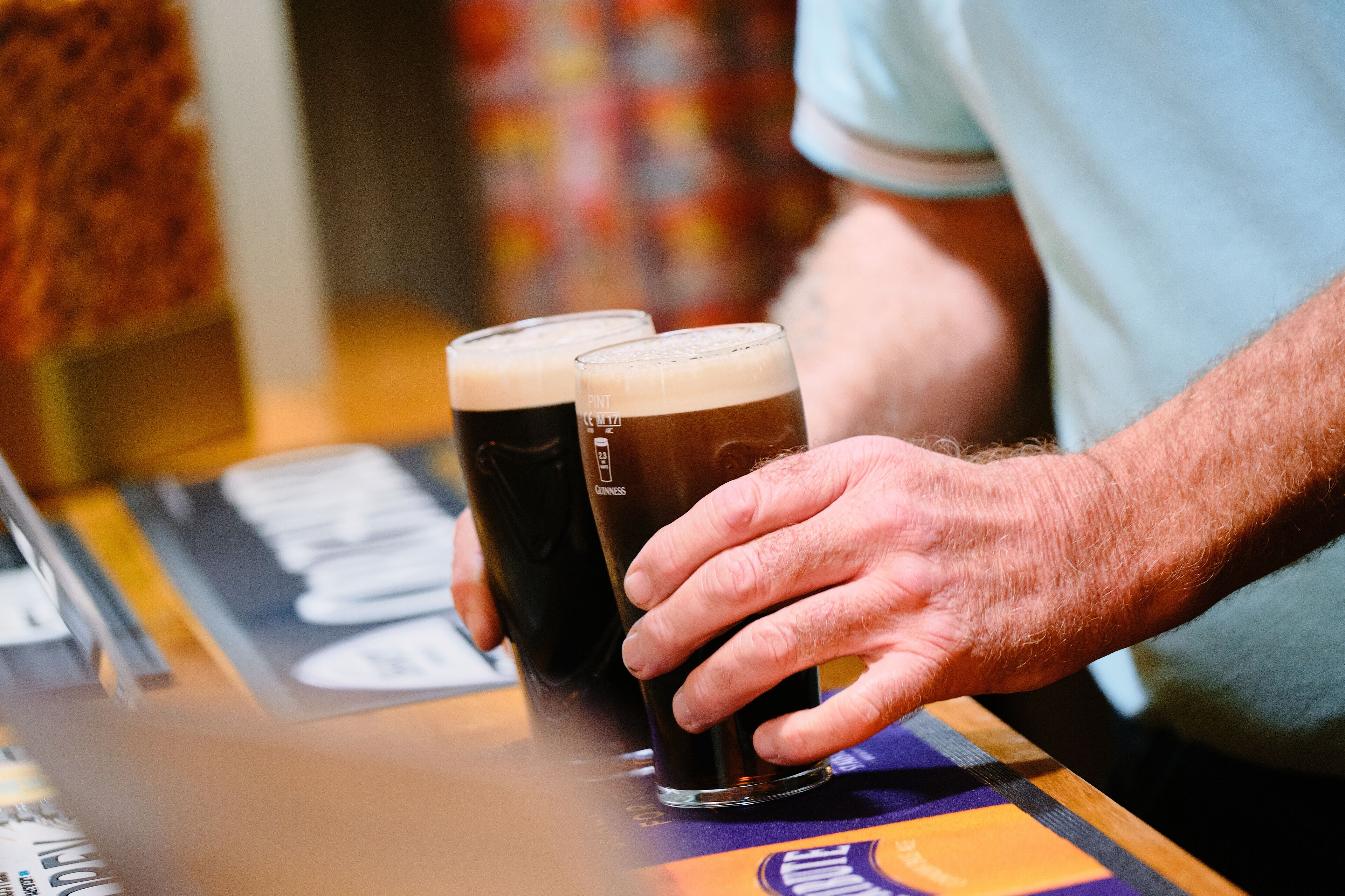A person holding two glasses of beer at a bar.