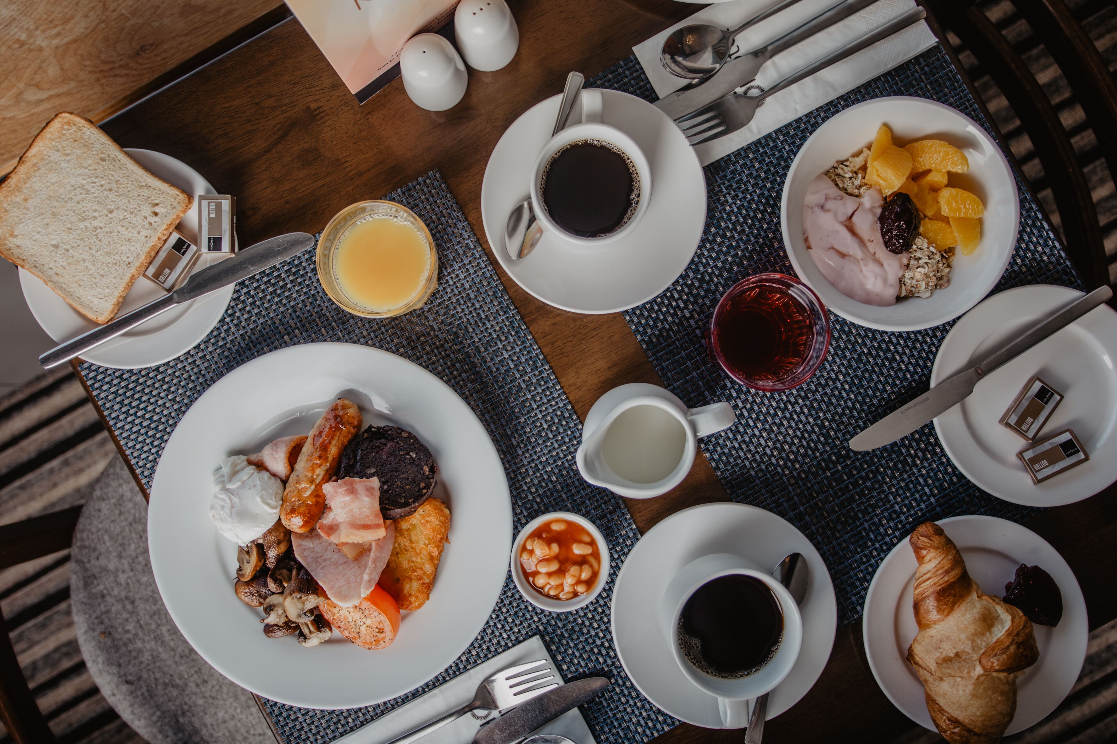 Une table mise pour le petit-déjeuner, avec des assiettes de nourriture, des tasses de café et un croissant.