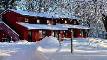 Un bâtiment rouge avec de nombreuses fenêtres et un toit recouvert de neige, entouré de neige.