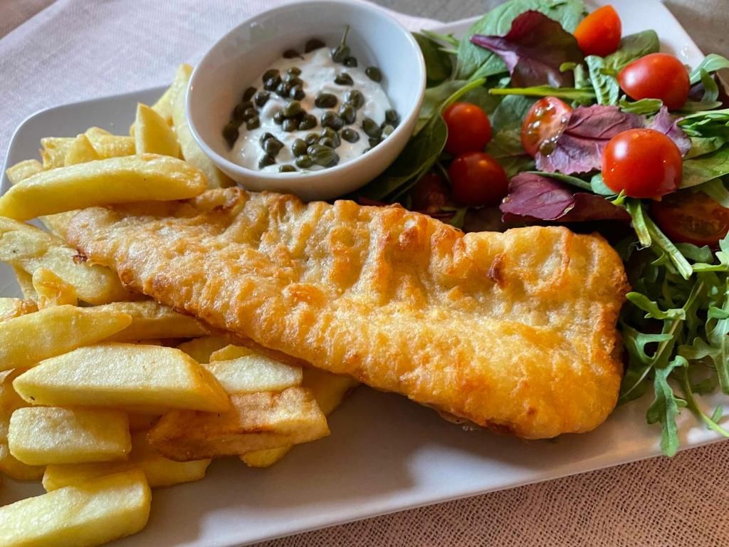 A plate with fish and chips, a salad, and a small bowl of sauce.