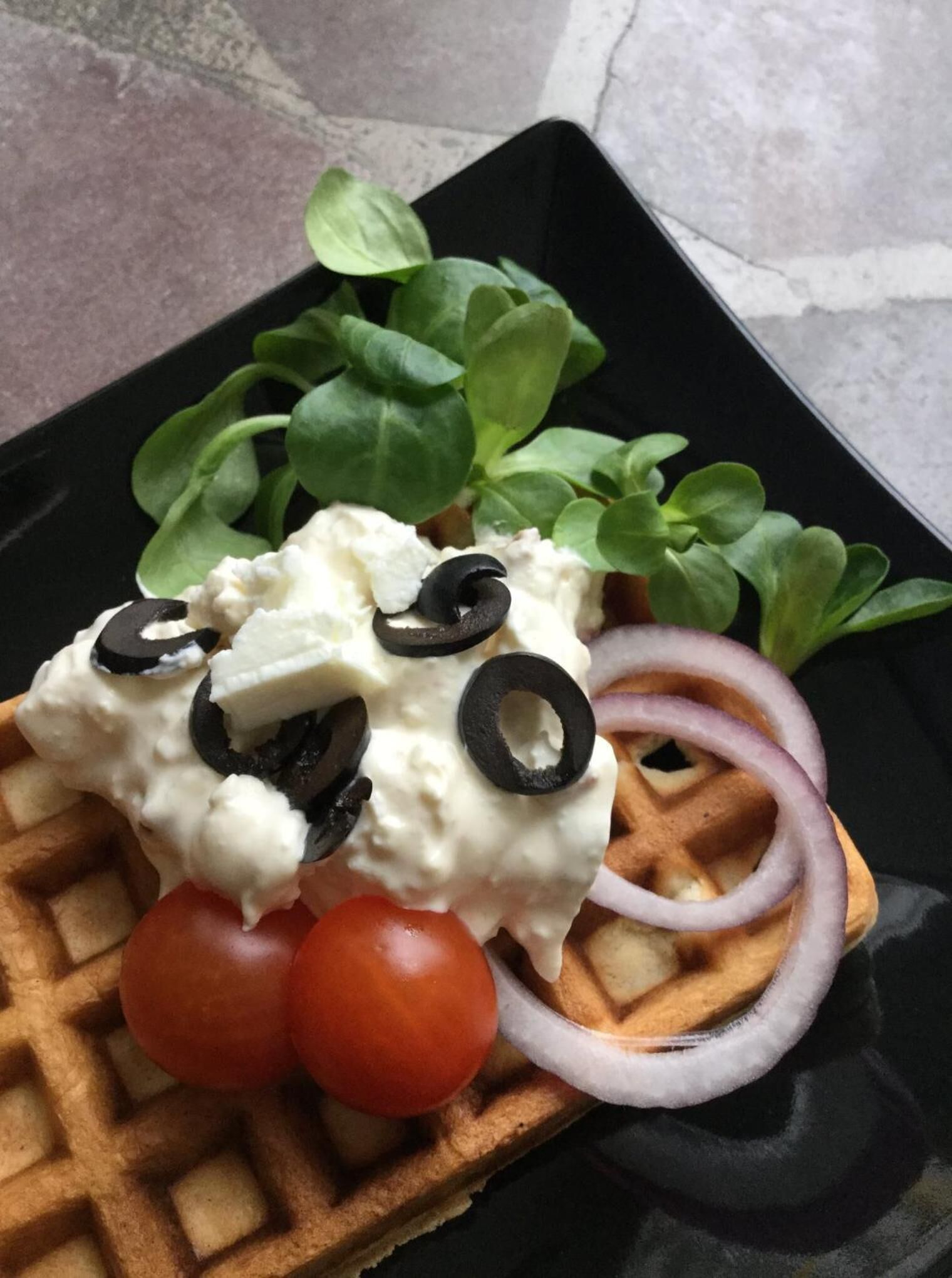 A waffle topped with whipped cream, black olives, and cherry tomatoes.