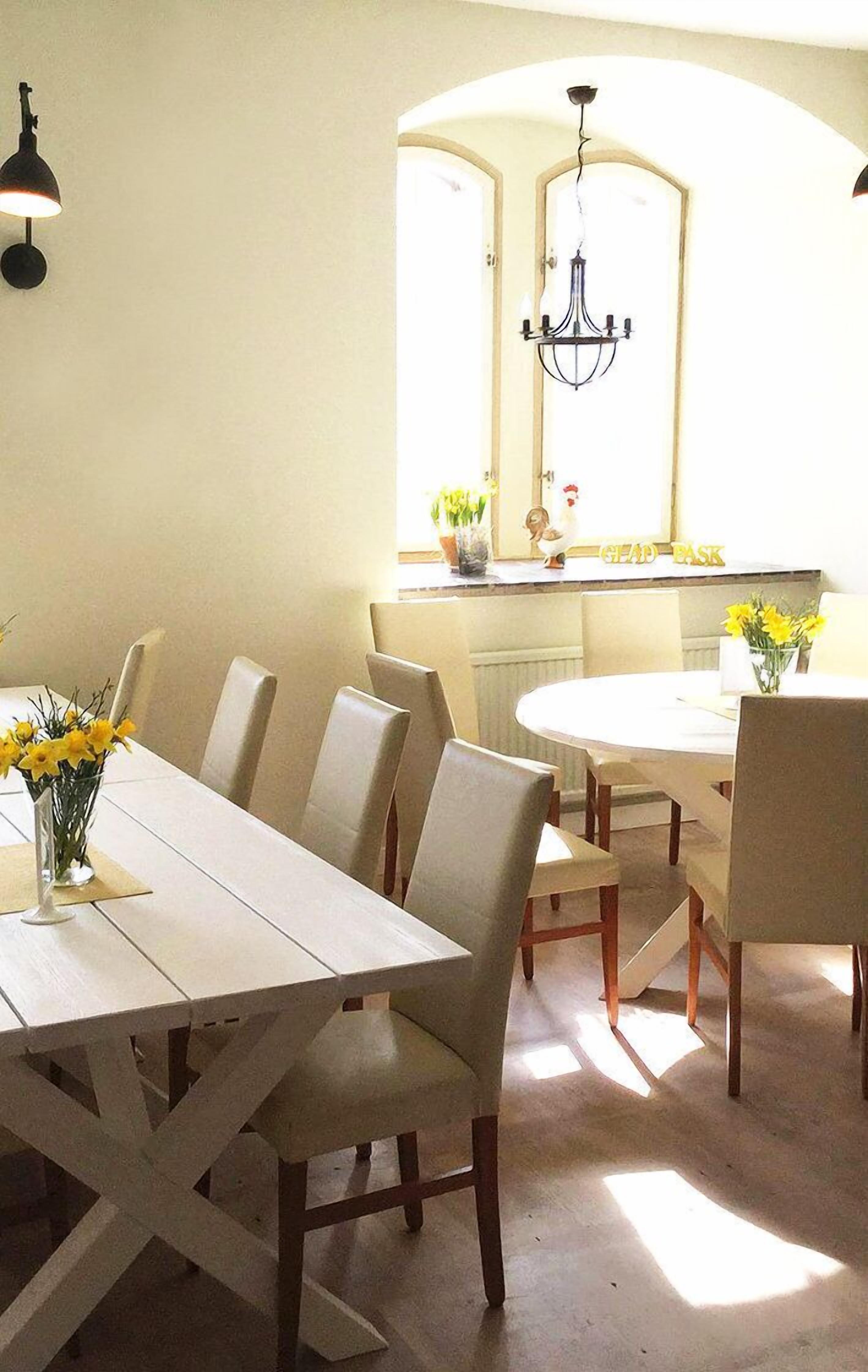 A dining area with a white table and chairs, a chandelier, and a window with natural light.