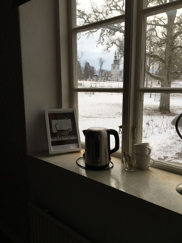 A window with a view of a snowy landscape, a kettle, and a framed picture on the windowsill.