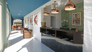 Un hall d’hôtel moderne avec un comptoir de réception en marbre, des luminaires suspendus, des œuvres d’art et une vue sur la salle à manger.