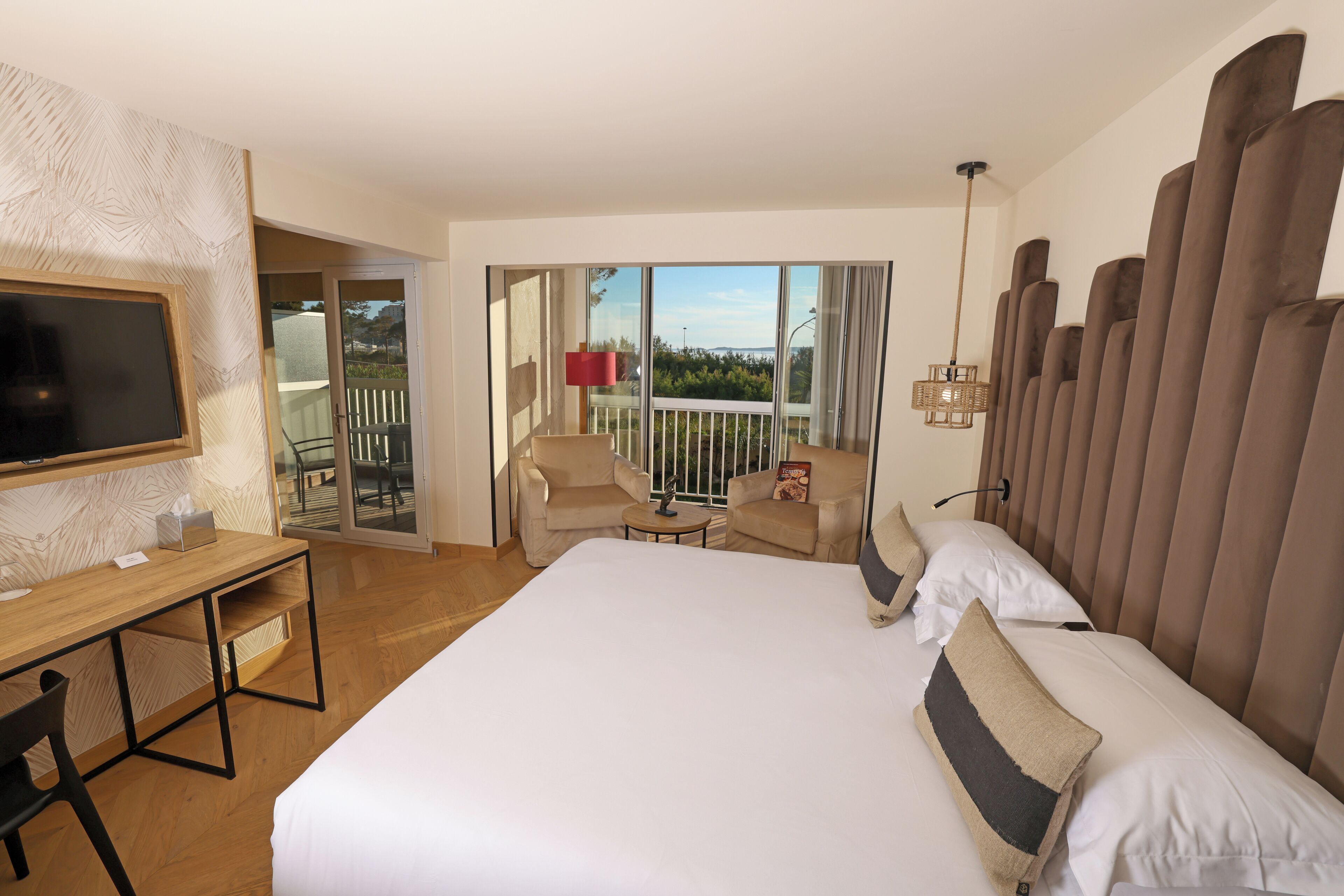 Habitación de hotel con una cama grande, un escritorio, una silla, una mesita, televisión y un balcón con vistas.