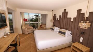 A hotel room with a large bed, a desk, a chair, a small table, and a view of the outdoors.