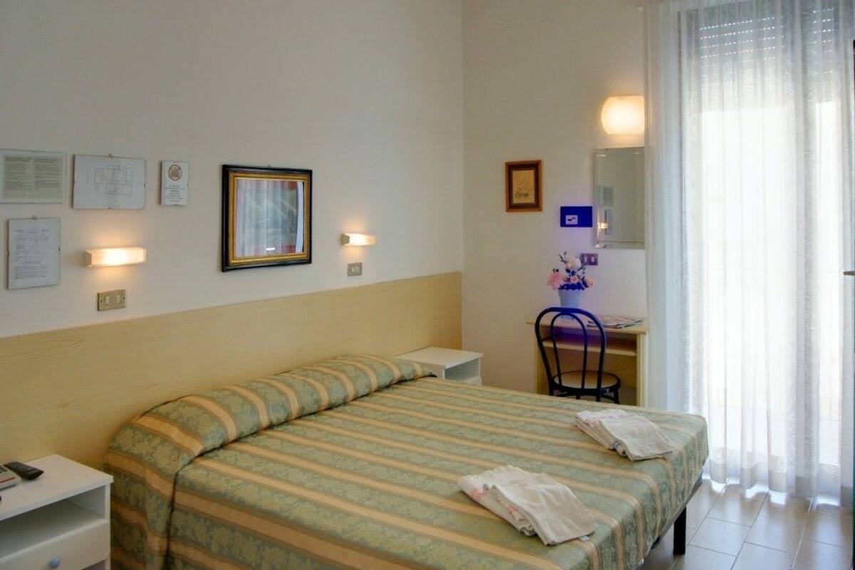 A hotel room with a bed, a desk, a chair, and a window with curtains.