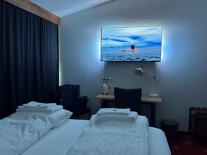 A hotel room with a bed, a desk, a TV, and a window.