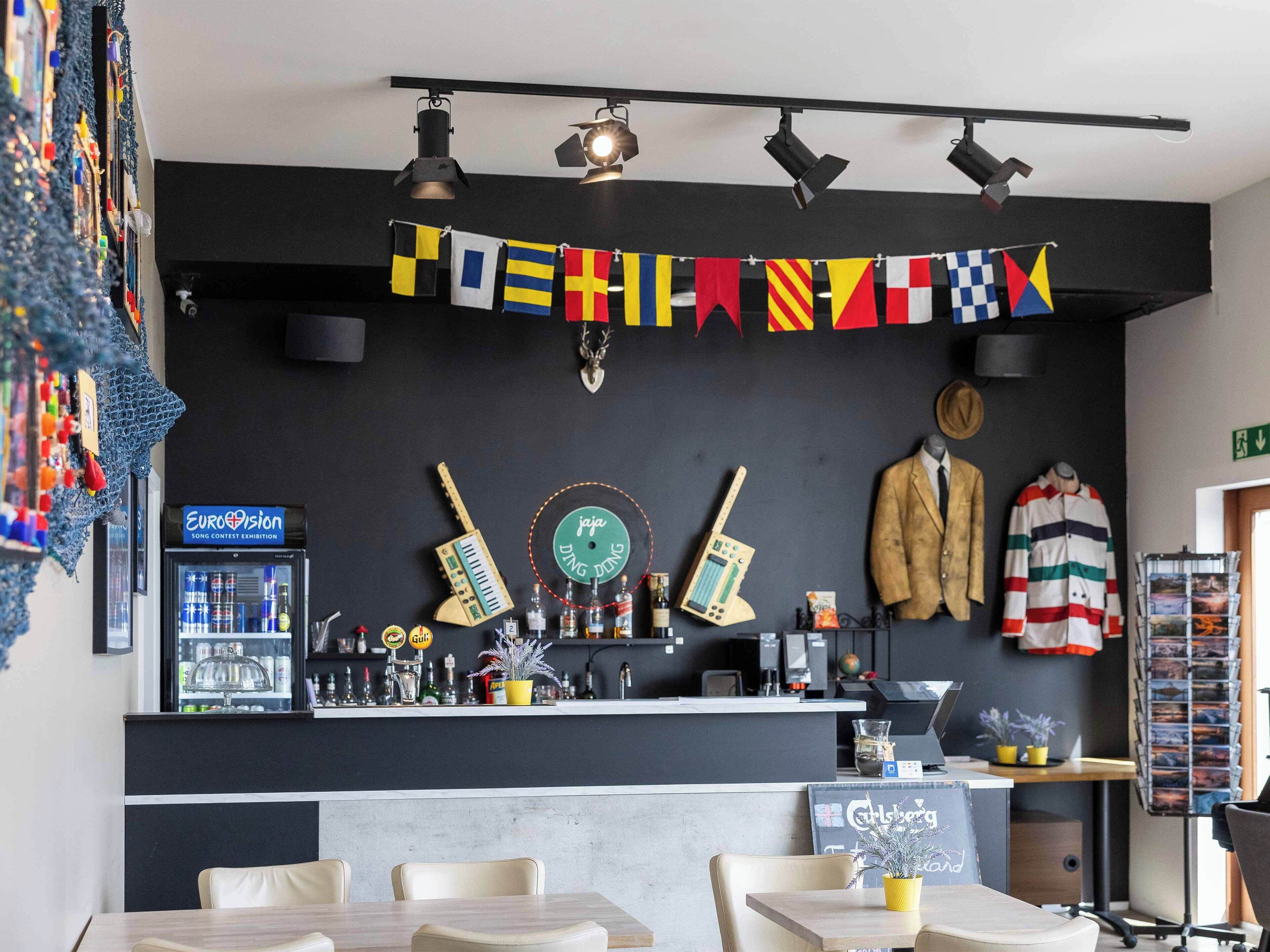 A bar area with a counter, multiple guitars, a jukebox, and a sign for a song contest exhibition.