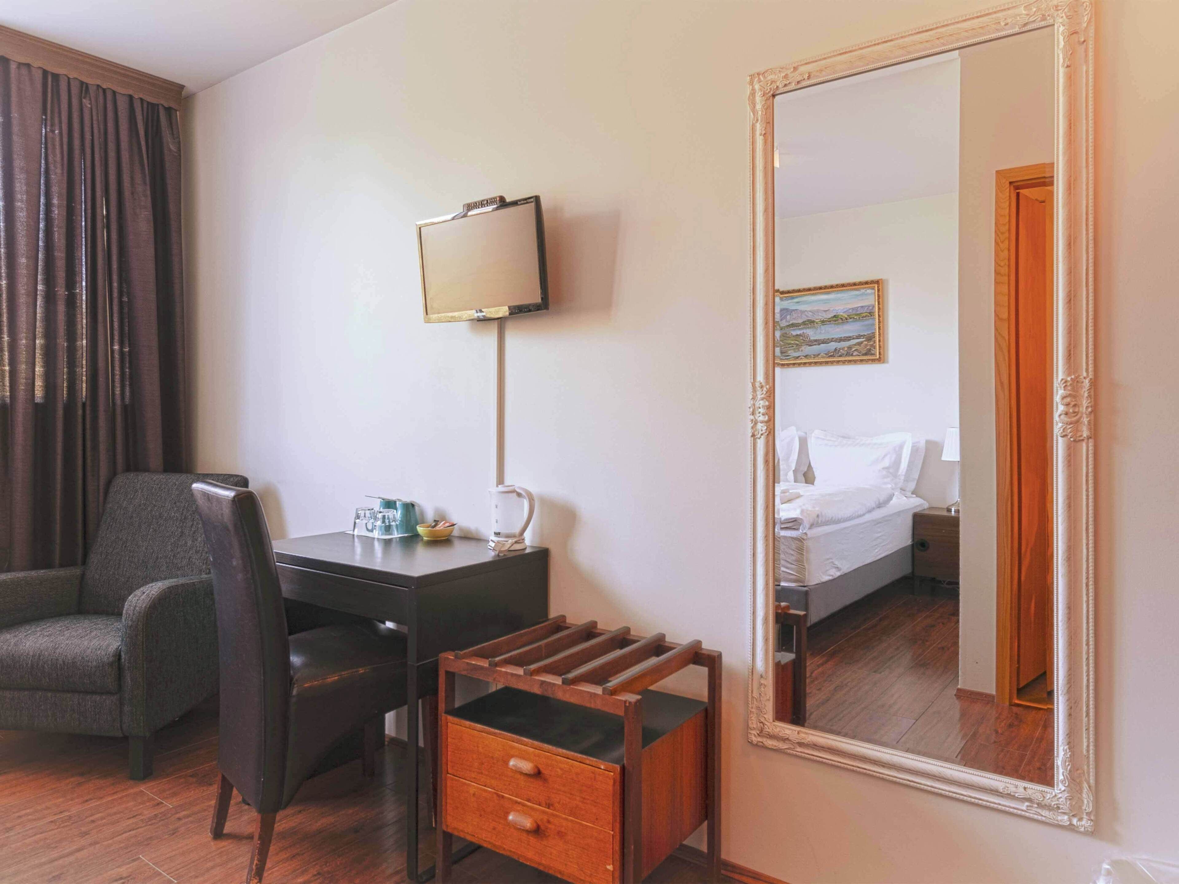 A hotel room with a desk, chair, and a large mirror.