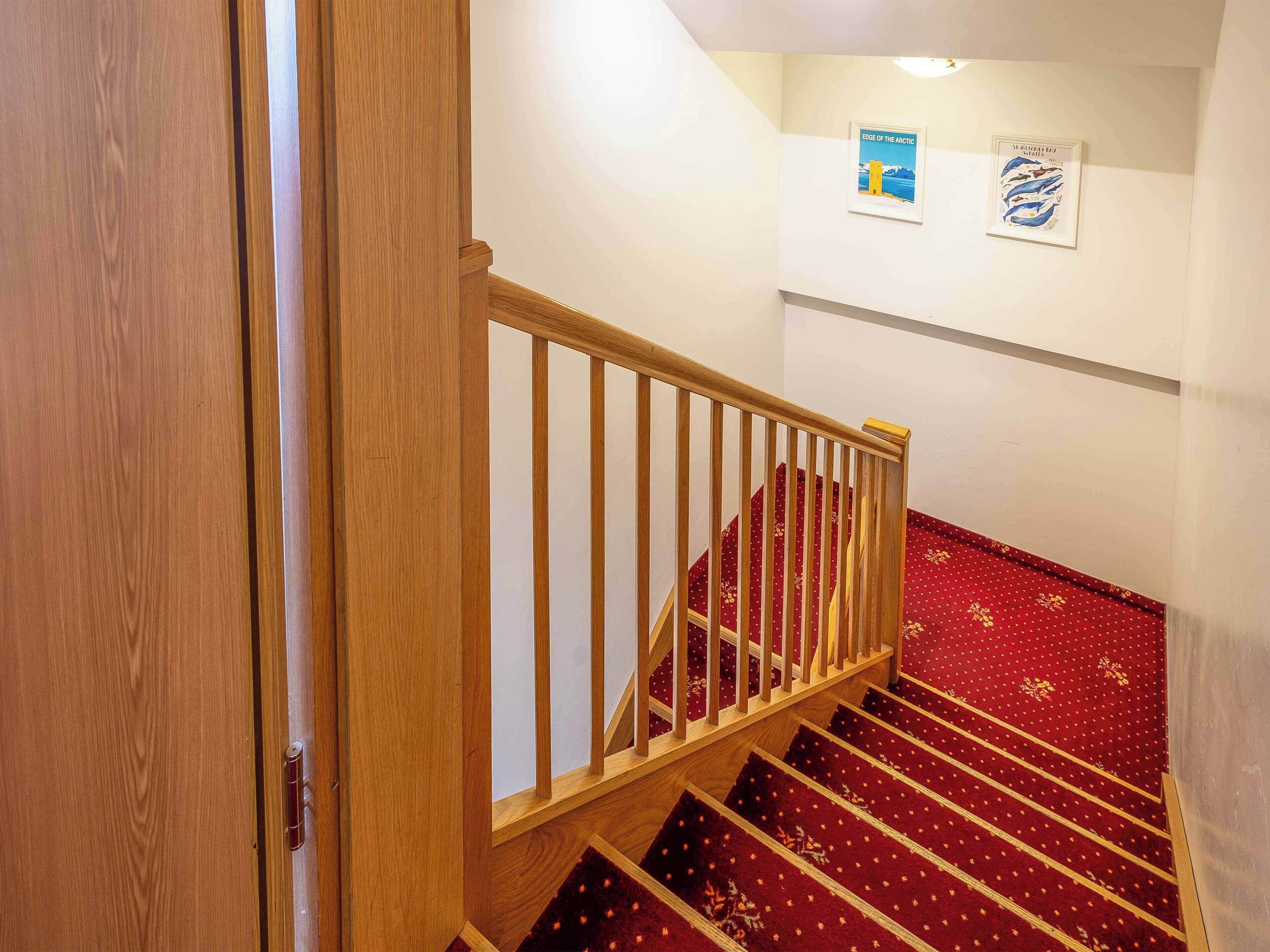 Un escalier en bois avec une petite plateforme recouverte d’une moquette rouge.