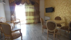 A spacious room with a large window, a flat-screen TV mounted on the wall, and a dining area with a round table and six chairs. - Hergla Diamond (Hergla)