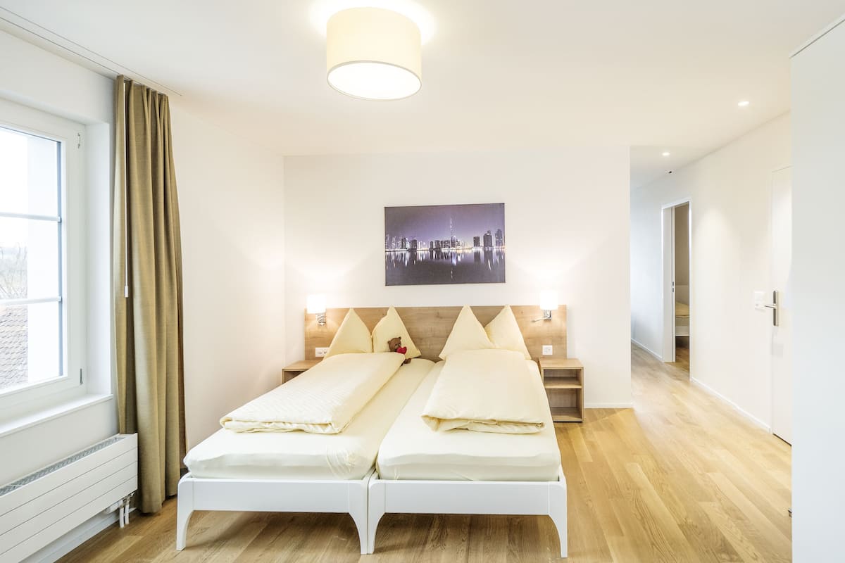 Camera d'hotel moderna con un letto matrimoniale, un quadro raffigurante un paesaggio urbano e vista sulla città dalla finestra.