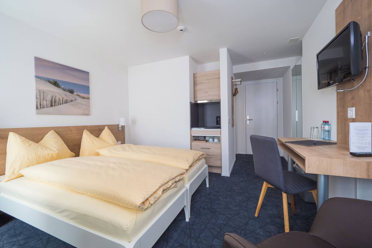 Una camera d'albergo con un letto, una scrivania, una sedia, una televisione e un quadro appeso al muro.