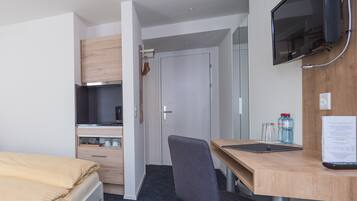 A hotel room with a bed, a desk, a chair, a television, a wardrobe, and a kitchenette.