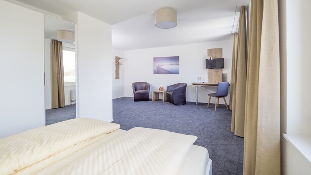A hotel room with a bed, two chairs, a desk, a TV, and a painting on the wall. - Hotel & Apartments Bären (Seengen)