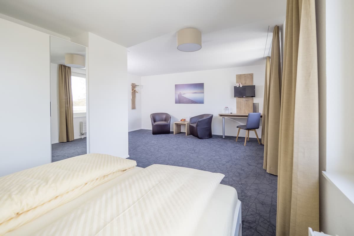Una camera d'albergo con un letto, due poltrone, una scrivania, una TV e un quadro appeso al muro.