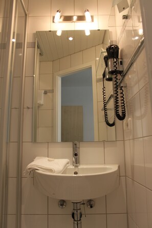 Ein Badezimmer mit einem weißen Waschbecken, einem Spiegel und einem an der Wand befestigten Föhn.