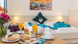 A breakfast setup with a table, plates of food, glasses of orange juice, and a bed with a heart-shaped pillow in the background. - Hotel Amenity München (Munich)