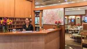 A reception desk with a wooden finish, a map on the wall, and a vase of flowers. - Hotel Amenity München (Munich)