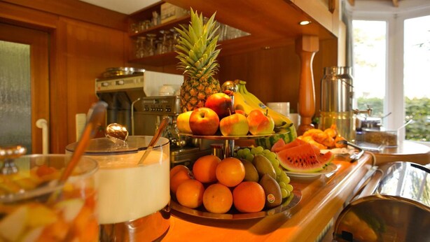 A breakfast buffet with fruits, a pineapple, and a milk jug. - Hotel Amenity München (Munich)