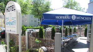 A hotel sign, outdoor seating area, and a blue umbrella with the hotel name. - Hotel Amenity München (Munich)