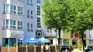A hotel with multiple floors, a large tree in front, and outdoor umbrellas. - Hotel Amenity München (Munich)