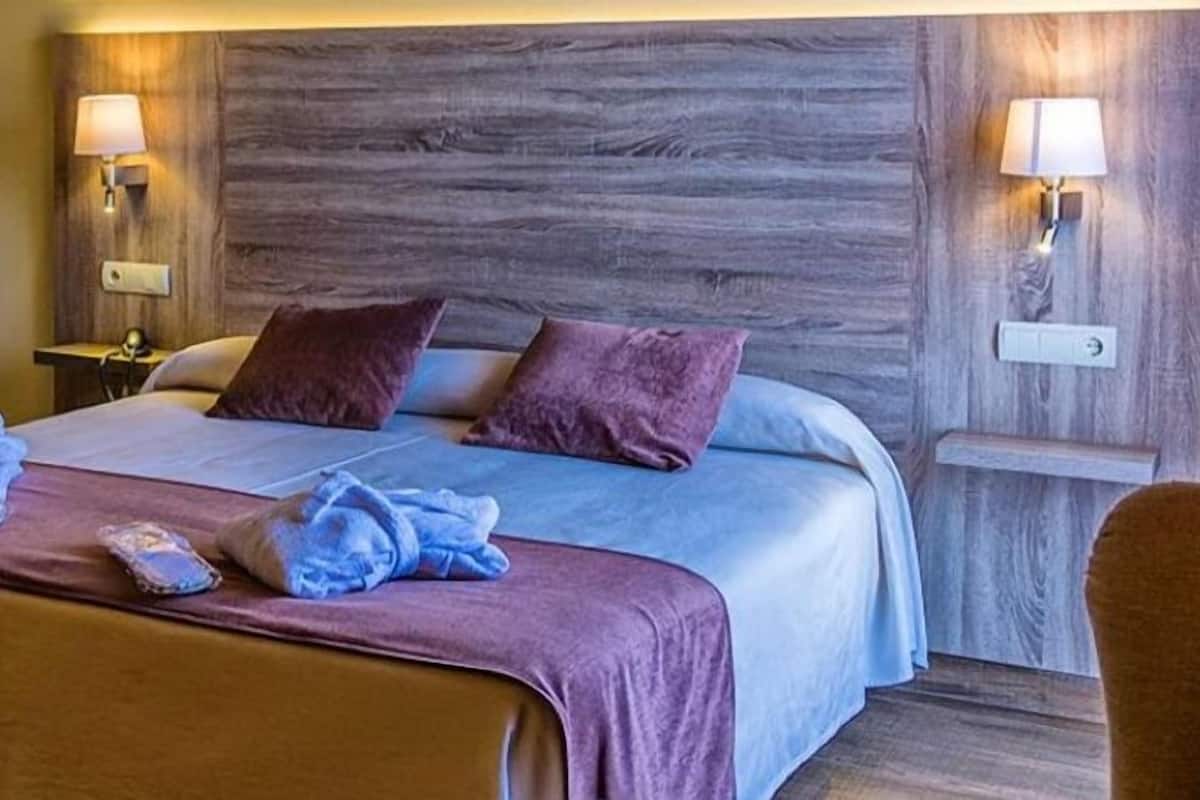 A hotel room with a large bed, two bedside lamps, a wooden headboard, and a small bedside table.