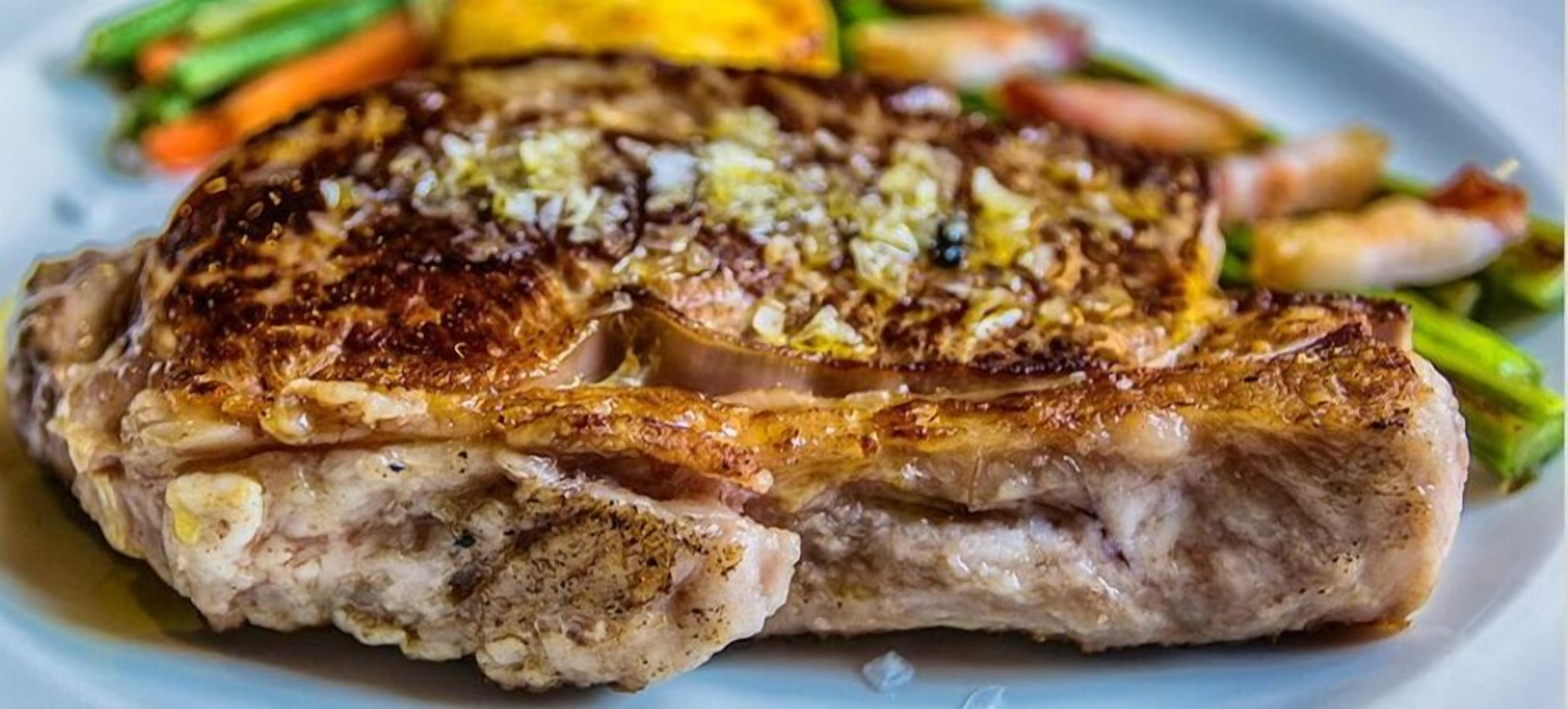 A steak with a crispy, golden-brown crust, served with vegetables and a sauce on a plate.