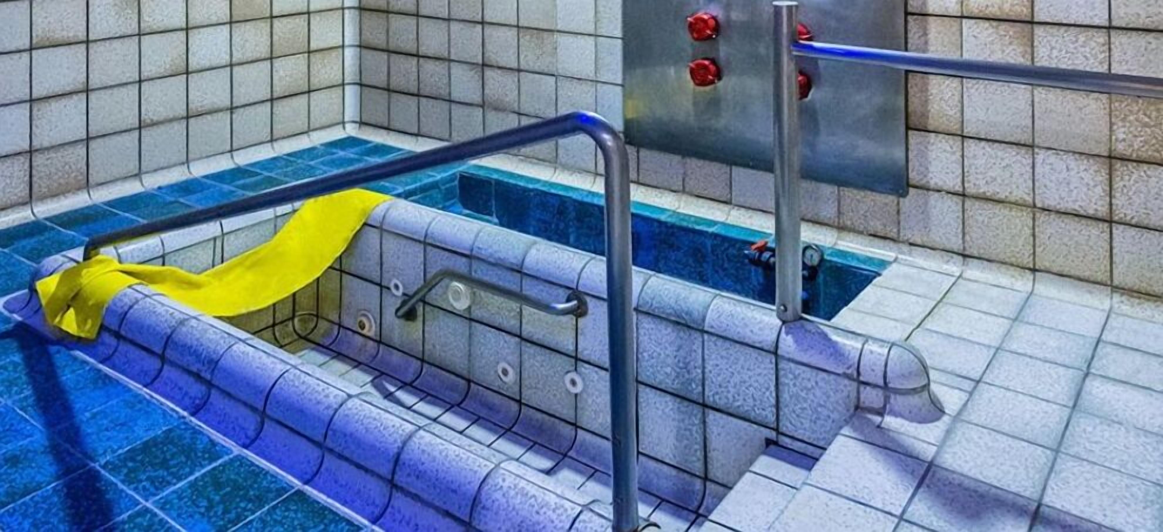 Zona de piscina con una cuerda de seguridad amarilla, barandillas metálicas y un panel de control con botones rojos.