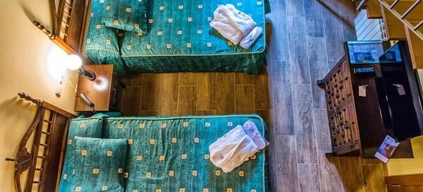 Een kamer met twee met groen bekleden bedden, een houten vloer, een houten kast en een tafeltje met een lamp.