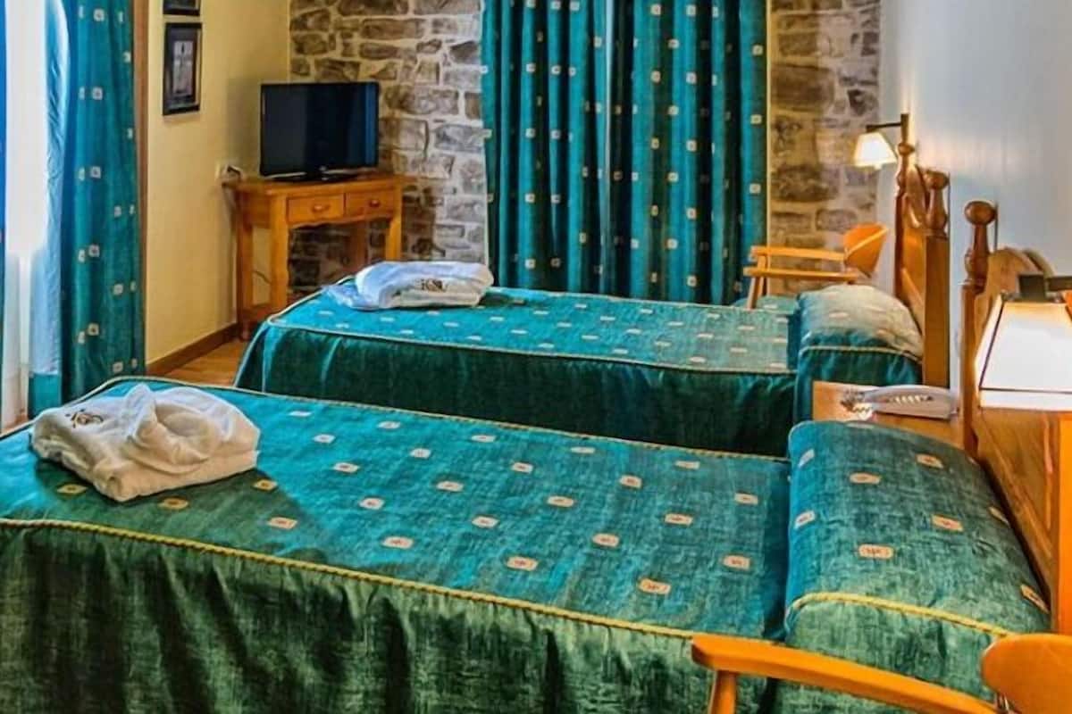 A room with two beds, a television on a wooden table, and a stone wall.