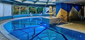 Een binnenzwembad met helderblauw water, een fontein in het midden en een betegelde vloer.