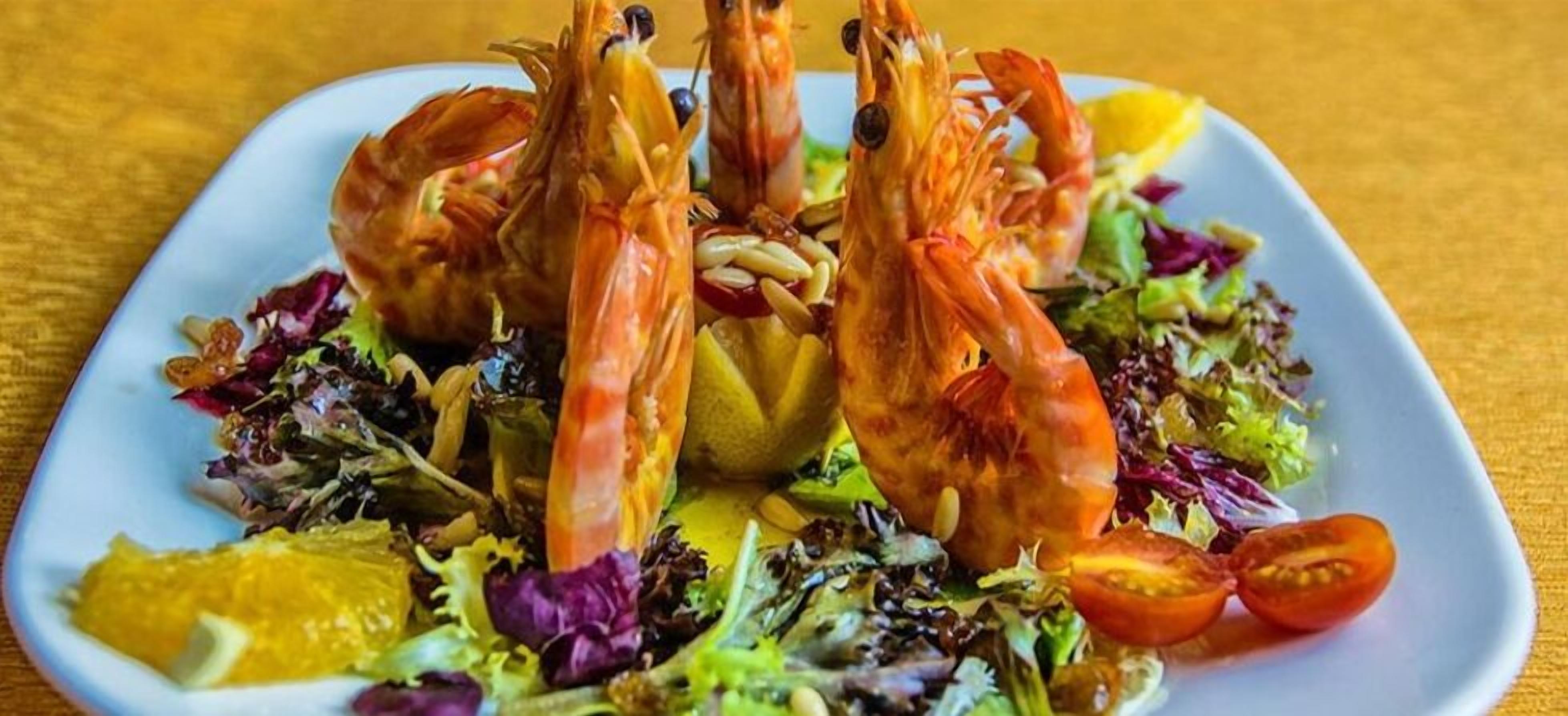 A plate of cooked shrimp with a salad and lemon slices.