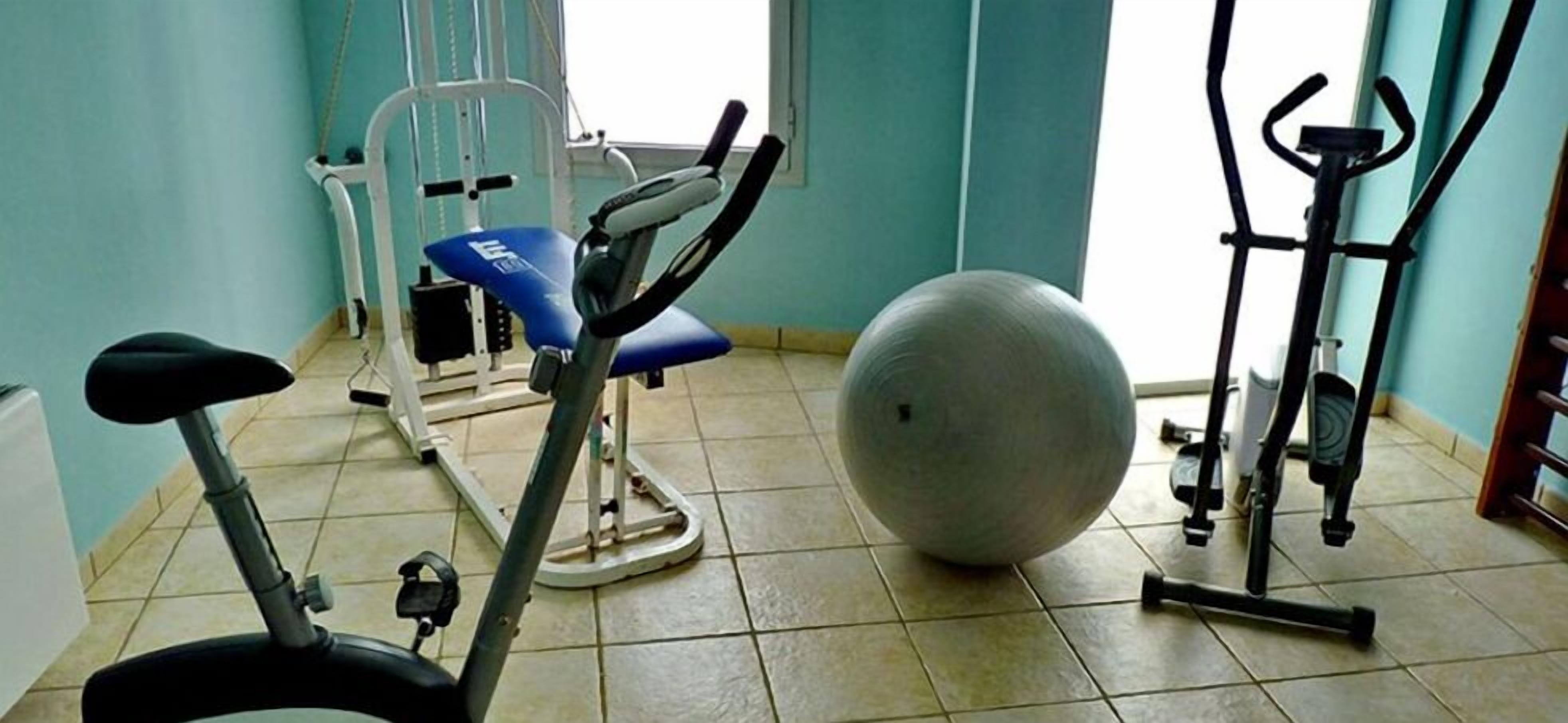 A fitness room with exercise equipment including a stationary bike, a rowing machine, an elliptical trainer, and a large exercise ball.