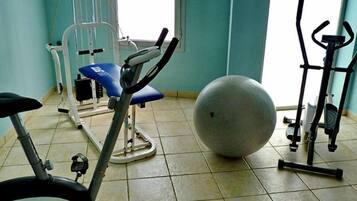 A fitness room with exercise equipment including a stationary bike, a rowing machine, an elliptical trainer, and a large exercise ball.