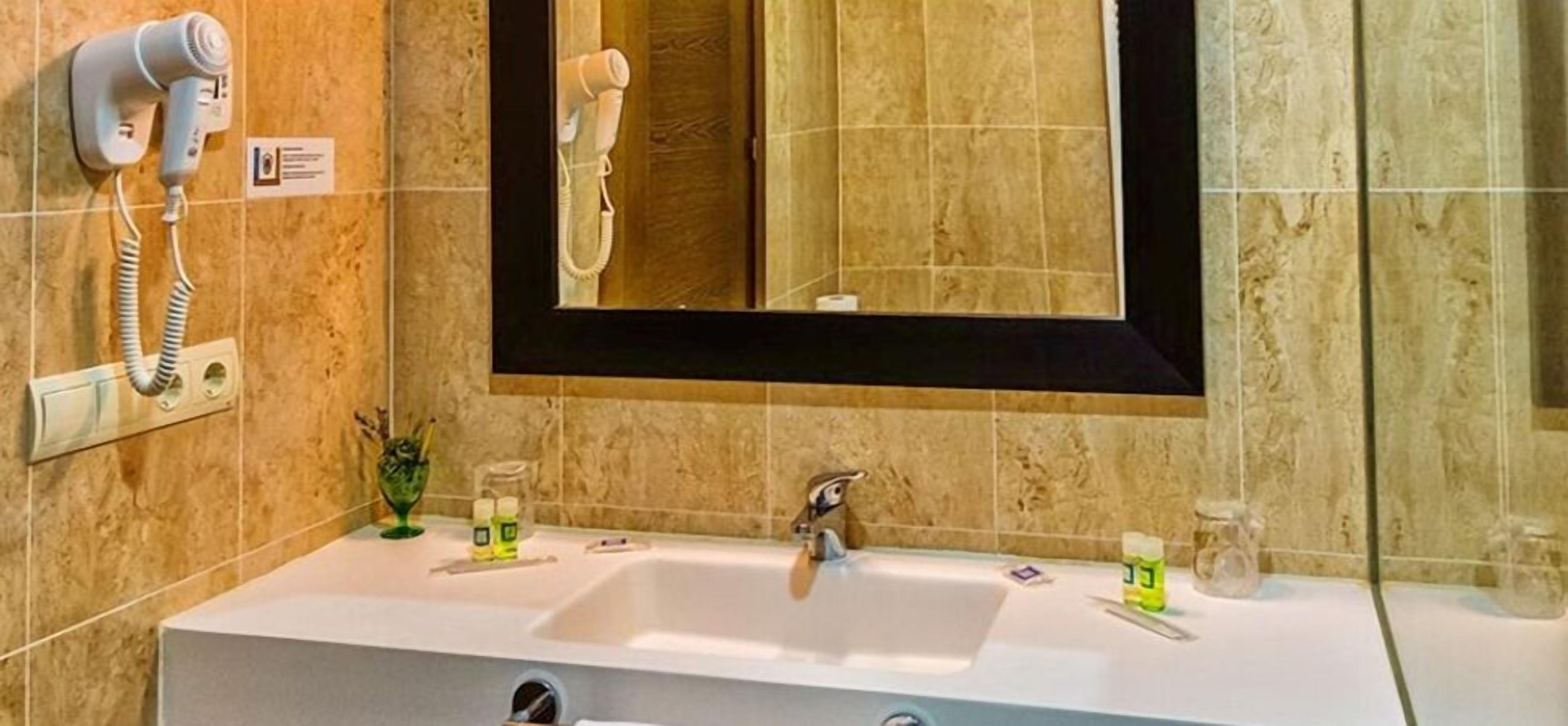 Un baño con un lavamanos blanco, un espejo y dos secadores de pelo fijados en la pared.