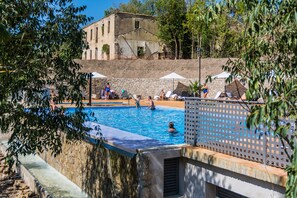A swimming pool with a water slide, surrounded by lounge chairs and umbrellas, with a stone building in the background. - Hotel Balneari de Vallfogona (Vallfogona de Riucorb)