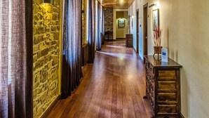 A hallway with wooden flooring, stone walls, and a wooden console table with a vase. - Hotel Balneari de Vallfogona (Vallfogona de Riucorb)