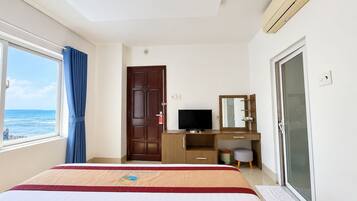 A hotel room with a bed, a desk with a television, a window with curtains, and a door.