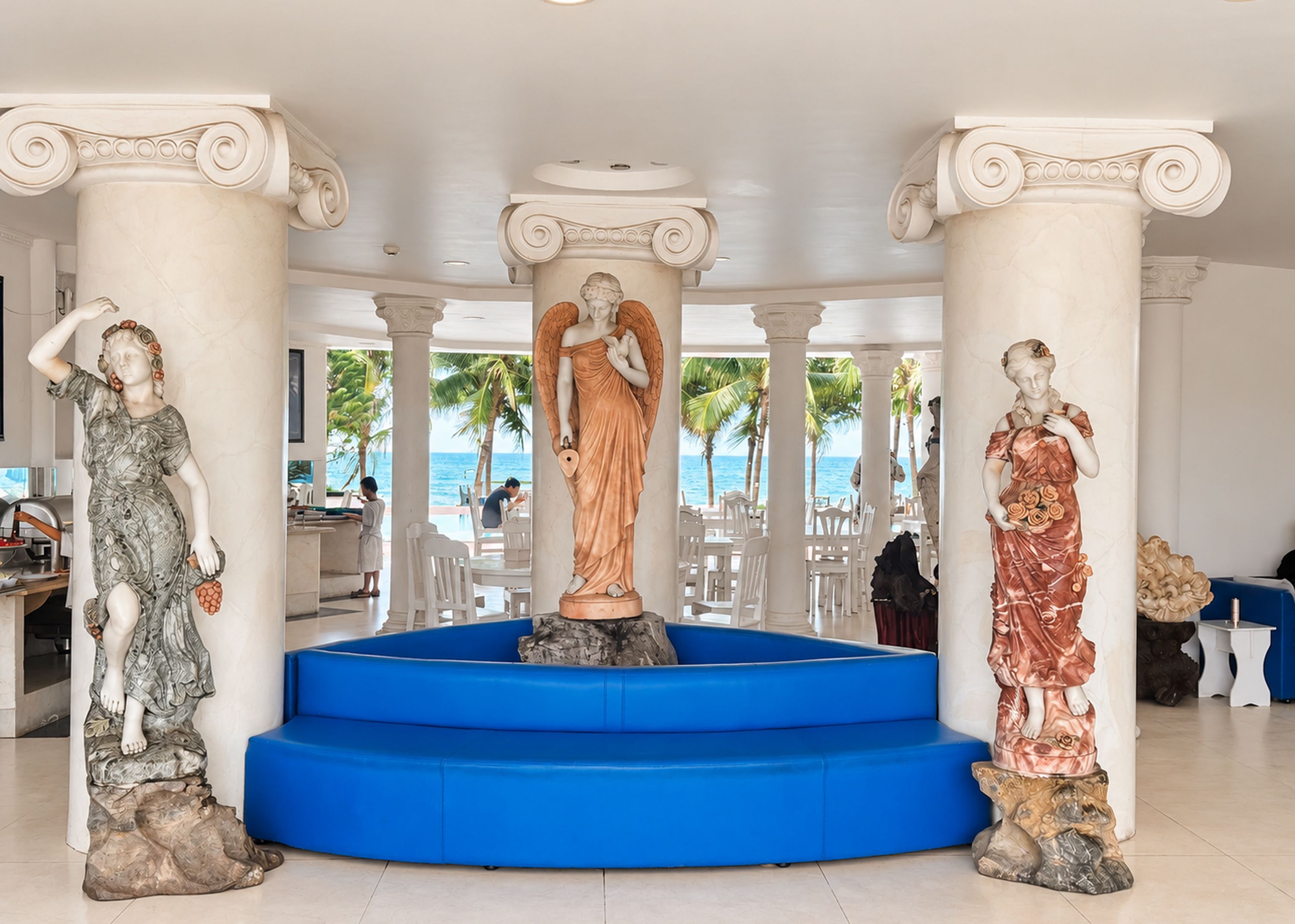 Un vestíbulo con tres estatuas, una escalera azul y vista a la playa.