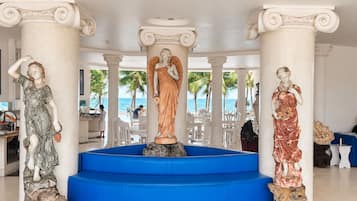 Un vestíbulo con tres estatuas, una escalera azul y vista a la playa.