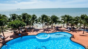 A pool with a circular center, surrounded by palm trees and lounge chairs, with a beach and ocean view. - Pacific Beach Resort (Mui Ne)