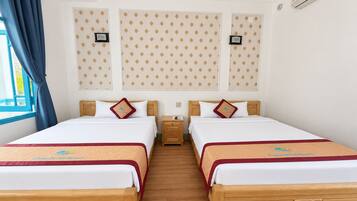 A hotel room with two beds, a wooden headboard, a nightstand, and a window with blue curtains.