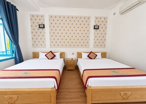 A hotel room with two beds, a wooden headboard, a nightstand, and a window with blue curtains. - Sunday Pacific Beach Resort Muine (Mui Ne)