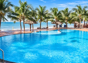 A clear blue pool surrounded by palm trees and lounge chairs, with a view of the ocean. - Sunday Pacific Beach Resort Muine (Mui Ne)