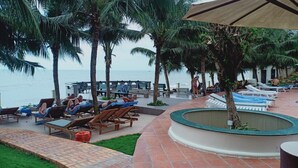 A resort pool area with lounge chairs and palm trees, overlooking the sea. - Pacific Beach Resort (Mui Ne)